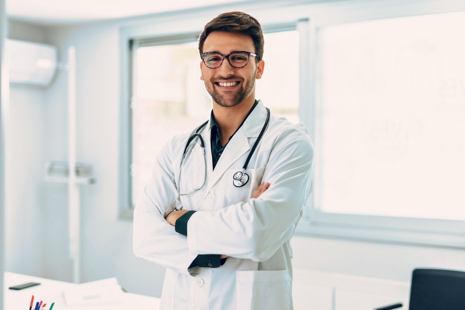 Handsome male doctor with stethoscope over neck working while looking at camera in the medical consultation.